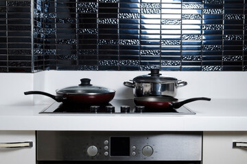 Frying pan on modern black induction stove. Energy efficient electric hob with built-in oven at...