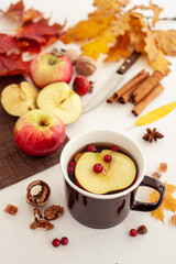 Autumn hot tea with apples and cranberry berries. A cup of tea among the fallen leaves on the white table.