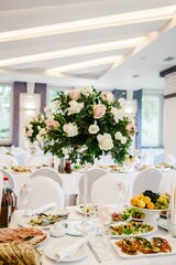 A composition of flowers and green is on a festive table at the wedding banquet hall. Stands candles. Close up.