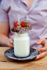 Detail of the handsome man holding milk shake cocktail in a glass bottle with biscuits, chololate...
