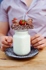 Detail of the handsome man holding milk shake cocktail in a glass bottle with biscuits, chololate and strawberry in a cafe. Outside. 