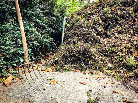 Used digging fork next to a pile of old leaves and garden rubbish during autumn