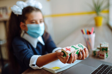 Wooden cubes Covid-2019 in the hand of schoolchild. Schoolgirl doing her homework with computer at home. Homeschooling during quarantine. 