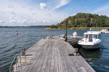 Wooden jetty pier berth Parking for yachts near the residence. A white yacht is moored at its own pier marina on a sunny summer day. Yachting people lifestyle. The Stockholm archipelago in Sweden.