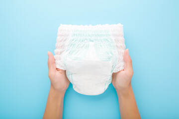 Young mother hands holding white baby diaper pants on light blue table background. Pastel color. Closeup. Point of view shot. Top down view.