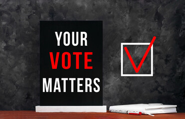 Your Vote Matters text sign on black chalkboard with white notebok and red pen on dark background....