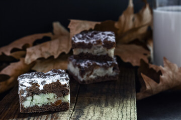 Three pieces of chocolate vanilla cookies with raisins lie on a board in the background a glass of milk and autumn leaves. Black, dark background.