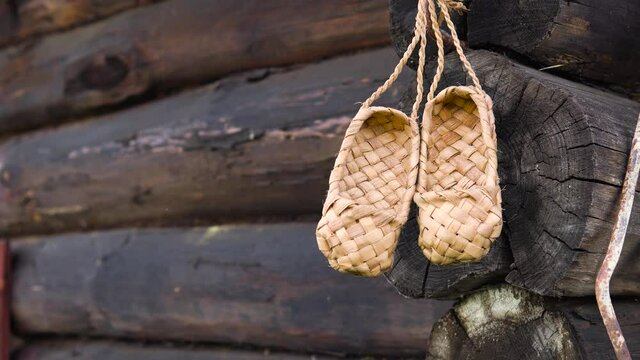 Rustic rural concept. Antique handmade rustic shoes - bast shoes. A pair of bast shoes hanging on the background of a wooden log wall.