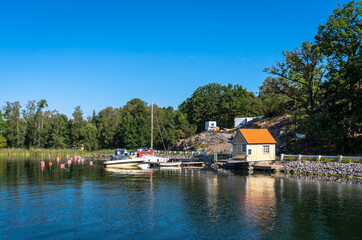 A small yellow wooden house on the shore. Marina berth for private yachts and boats. Jetty for ships near the Coast Of Sweden. The Stockholm archipelago. Active lifestyle yachting.