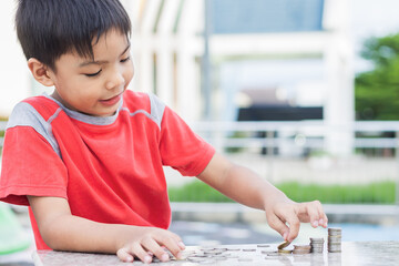 Portrait of happy Asian child boy counting the coins. Childhood put the money on the table. Kid saving money for the future concept. Children learning.