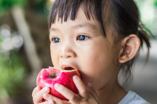 Portrait​ image​ of​ 1-2​ yeas​ old​ of​ baby.​ Happy​ Asian child girl eating and biting an red apple. Enjoy eating moment. Healthy food and kid concept.​ Vintage​ style.