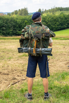 A Germany scout man in uniform and beret gathered for trekking or hiking. A scout with a large backpack on his back. Packing equipment for a hike. Collected big backpack rucksack and tourist axe. © GenоМ.