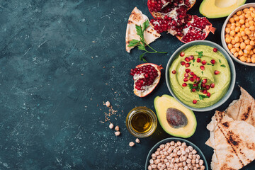 Homemade green hummus with avocado, parsley, olive oil, pita, raw chickpeas, pomegranate on dark background. Middle eastern, jewish, arabic cuisine. Top view. Copy space. Vegan, vegetarian food