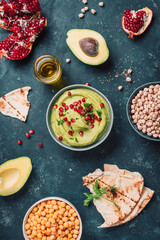 Homemade green hummus with avocado, parsley, olive oil, pita, raw chickpeas, pomegranate on dark background. Middle eastern, jewish, arabic cuisine. Top view. Copy space. Vegan, vegetarian food
