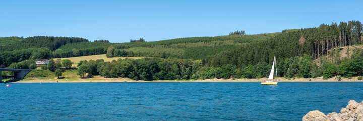 View of the "Biggesee" or "Bigge Reservoir" in Germany. The sailing yachts swimming on the surface. The blue sky is reflected in the water. Beautiful landscape of the lake surrounded by forest banks. 
