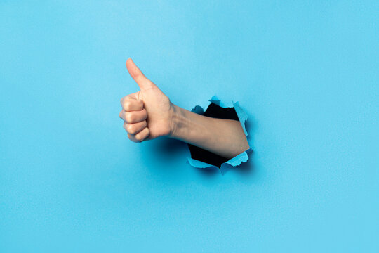 Hand makes thumbs up gesture on blue background. The gesture is all good, like