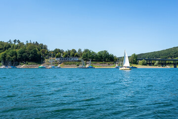 View of the "Biggesee" or "Bigge Reservoir" in Germany. The sailing yachts swimming on the surface. The blue sky is reflected in the water. Beautiful landscape of the lake surrounded by forest banks. 