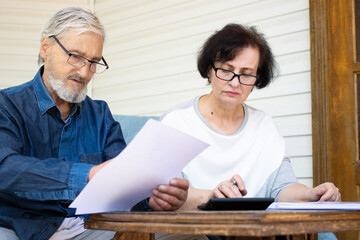 Serious focused mature couple reading paper documents and calculating bills to pay or checking...