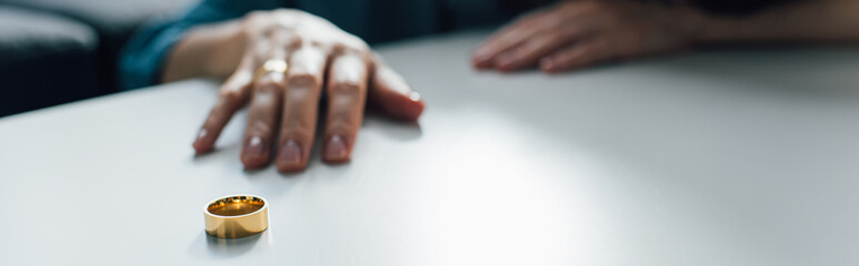 panoramic crop of woman reaching golden ring on coffee table, divorce concept