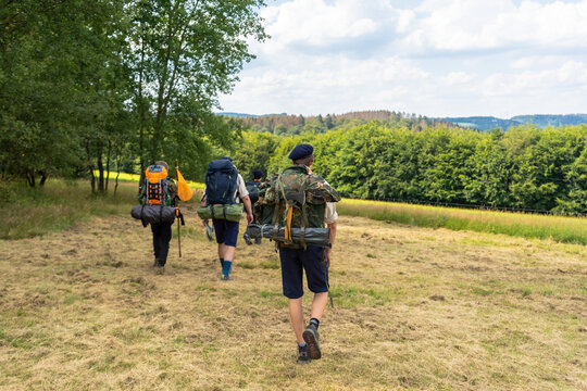 Scouts or tourists go with big backpacks on the green forest trail on sunny summer day. Active healthy lifestyle people with rucksacks. Hiking Trekking Scouting. Green forest background.