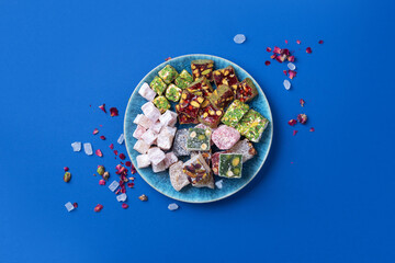 Middle Eastern sweets. Turkish delight with pistachios nuts on plate over blue background. Top...