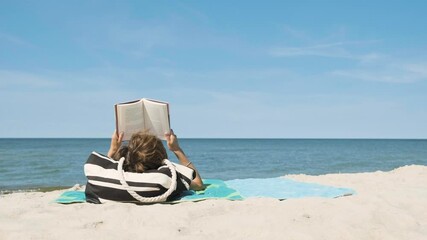 Anonymous woman from behind sunbathing on the beach and reading a book in summer day
