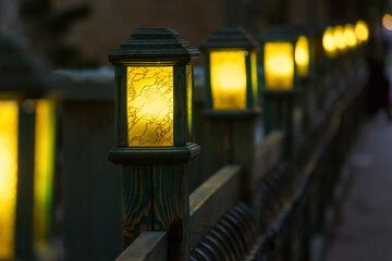 wooden street lamps with yellow glass diffuser on wooden fence of backyard, old light pole glow warm at evening closeup in perspective, nobody.