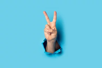 Fotobehang Male hand makes a two fingers up greeting gesture on a blue background. Banner © Alex