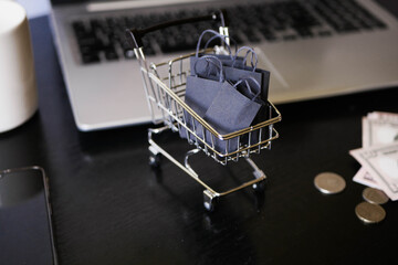 Shopping cart with bags stand on the table near laptop. Black friday. Sale announcement. E-commerce business. Ordering  in the internet store 