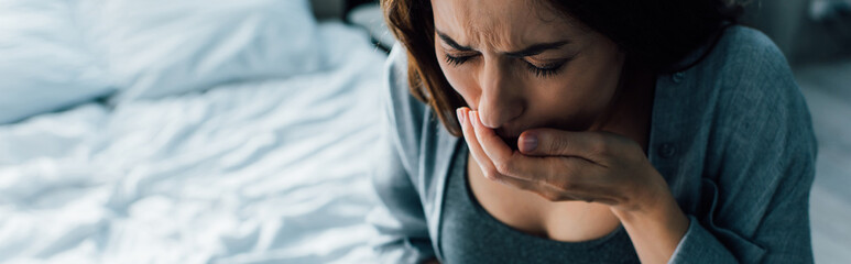 panoramic crop of woman covering mouth while having nausea at home