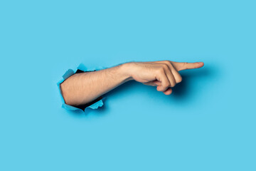 Hand points to something on a blue background. Gesture look at this, pay attention