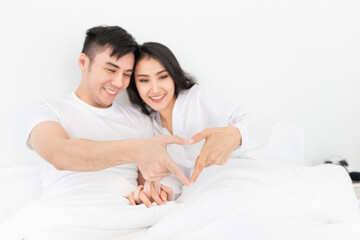 Obraz na płótnie Canvas close up hands, Asian lover show heart sign with hand, they feeling happy and smiling, they rest on bed, happiness honeymoon