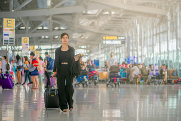Traveling concept. Asian businesswoman walking with a luggage at airport terminal and airport terminal blurred crowd of travelling people on the background.
