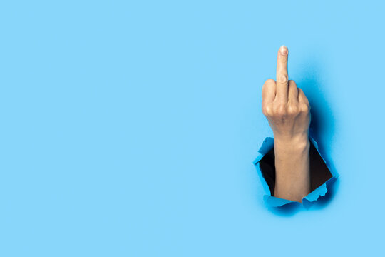 Hand shows the gesture of the middle finger on a blue background. Offensive gesture, fuck off, leave me alone