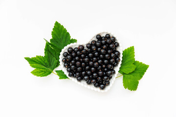 Black currant berries in a white plate in the form of a heart on a white background.