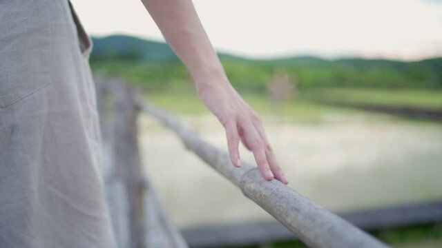 close up light skin female hand touch and sliding over wooden bridge hand railing, walking in Asian agricultural farm village, plantation field blur background, relaxing holiday vacation, non urban