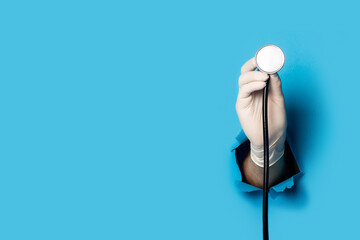 Man's hand in a medical glove holds a stethoscope on a bright blue background