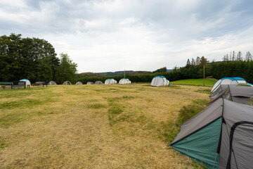 Scout camping. Army military tent close up in the base camp. Lots of  tents stand on a field against a green forest. 