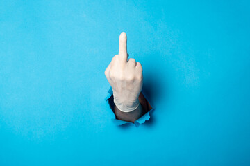 Man's hand in the medical glove showing middle finger on a bright blue background.