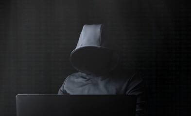 Hacker in a gray hood with a laptop on a dark background.