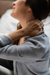 cropped view of brunette woman suffering from neck pain in bedroom