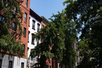 Fototapeta na wymiar Row of Colorful Old Residential Buildings in the East Village of New York City with Fire Escapes and Green Trees during Summer
