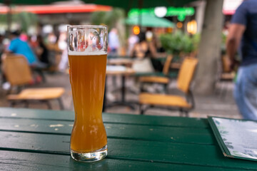A tall glass of light beer in a beer restaurant. Cafe outdoors on the street. On the green table is a mug of cold beer and a menu. Pub bar restaurant concept.