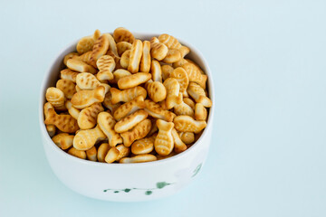 Mini fish shaped crackers heap in the white porcelain plate on light blue surface with copy space