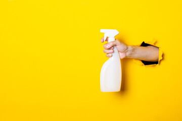 Hand holds spray with cleaning agent or water on yellow background