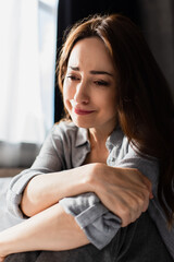 upset and brunette woman touching hand while sitting and crying at home