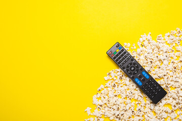 TV remote control, TV tuner or audio system and popcorn on a yellow background. Concept series,...