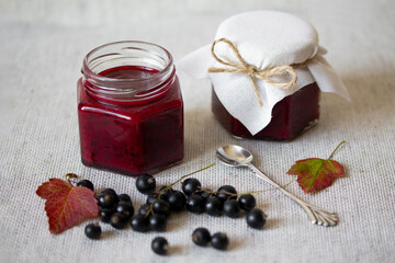Black currant jam in glass jars. Fresh berries with leaves and stems. Autumn harvesting and preserves. Organic food. Still life photography