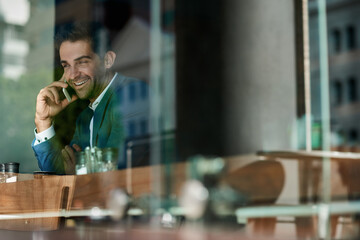 Smiling businessman talking on his cellphone by a cafe window
