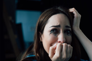 brunette woman with flowed mascara crying and looking away at home